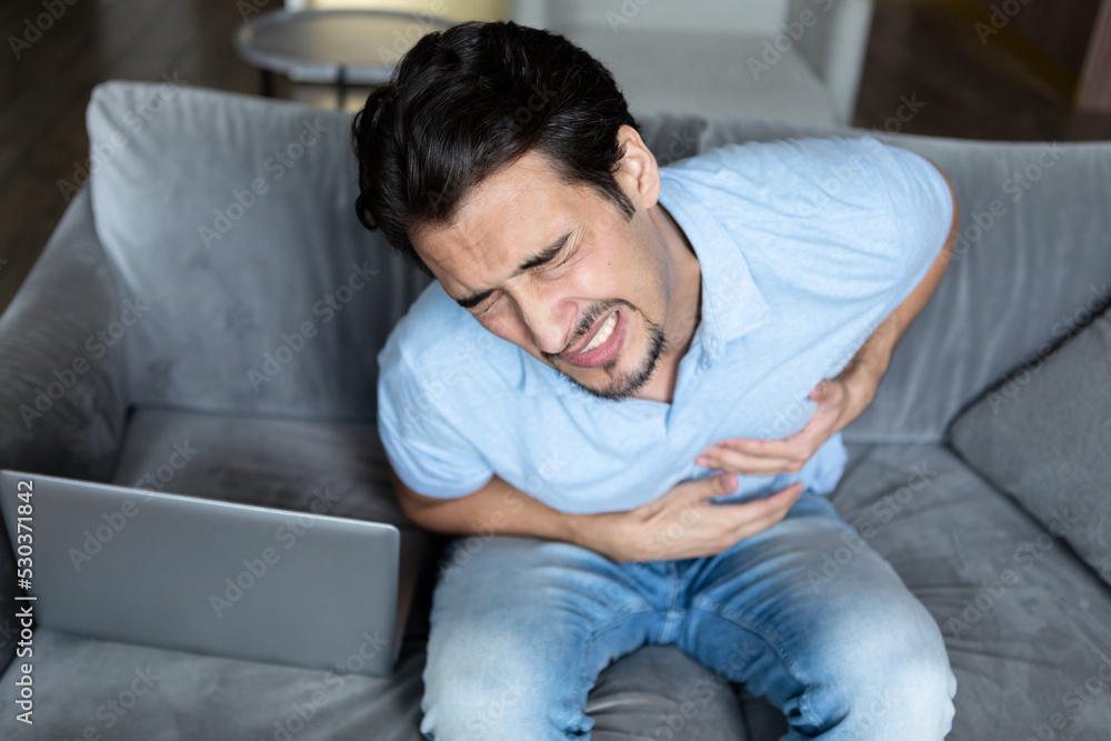 Top view on sick man sitting on the couch and holding his chest. Heart attack and illness concept