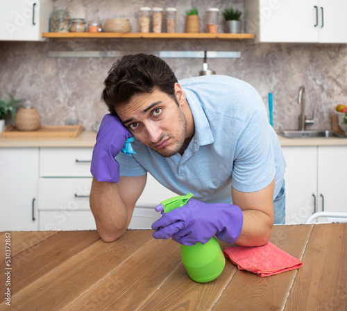 Tired and bored man cleaning table in the kitchen after cleaning house. Exhausted household concept