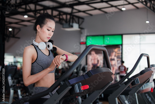 Asian woman setting up watch before runing on treadmill at fitness gym club. Sportswoman checking results on smartwatch after running.