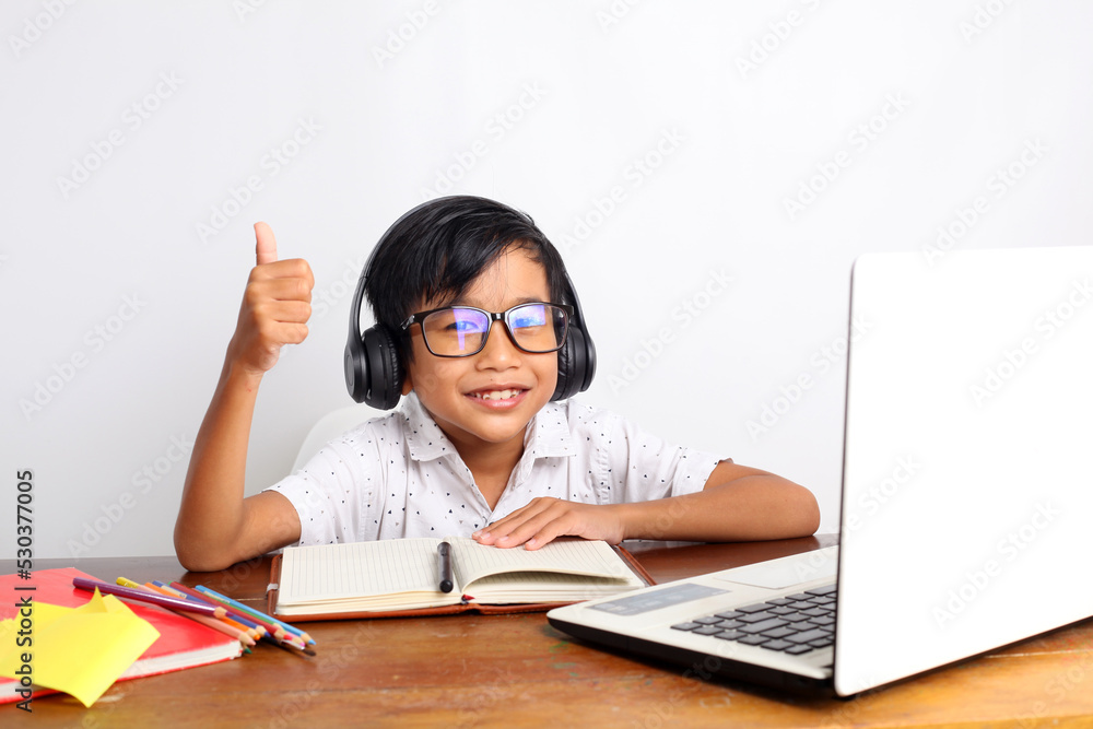 Happy asian elementary student studying with laptop at home and showing thumbs up. Isolated on white Happy asian elementary student studying with laptop at home and showing thumbs up. Isolated on white