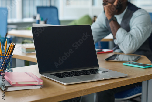 Laptop with black screen on workplace of modern office worker or employee on background of young African American manager