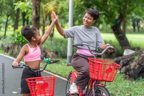 family activity concept Asian mother riding a bicycle with her half Asian African American daughter, happy children cycling in the park with mother together. photo