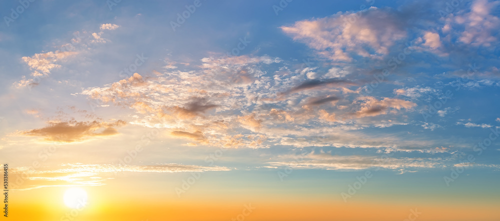Settind sun low in the yellow blue evening sky. Light translucent orange clouds in the sunset heaven. Picturesque calm sundown skyscape. Idyllic vanilla sky wide panorama. Weather forecast.