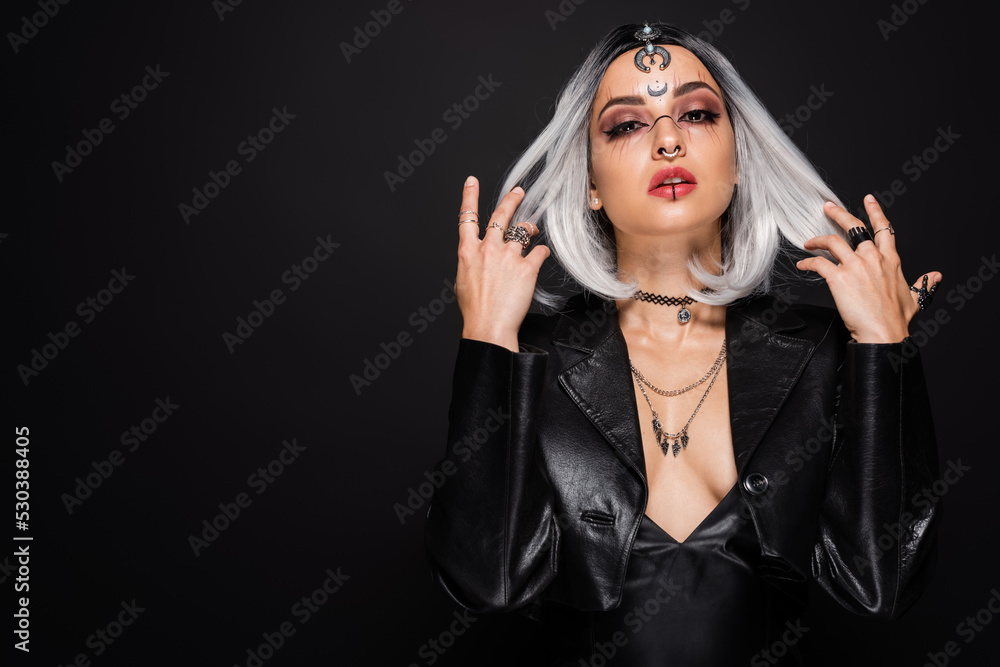 woman in witch costume and makeup touching ash blonde hair while looking at camera isolated on black. woman in witch costume and makeup touching ash blonde hair while looking at camera isolated on black.