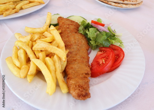 Fish and chips. Deep fried fish filet with french fries served on white plate with vegetables