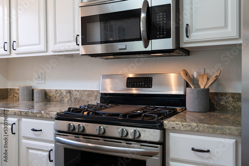 Modern kitchen details of gas stove with microwave above, stone counter tops and white cabinets.