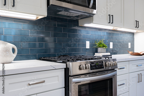 Modern kitchen details of white marble counter, gas stove, and blue tile backsplash.