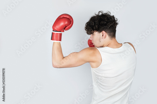 A teenage boy is boxing on a light background in boxing gloves, delivering a powerful downward blow to an imaginary opponent, the concept of teenage and youth sports, sports advertising