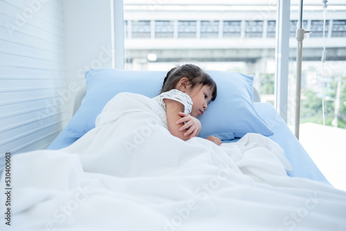 Asian girl patients are sad and lying-in patient's bed with alone, On white wall background, to children health care and health insurance concept.