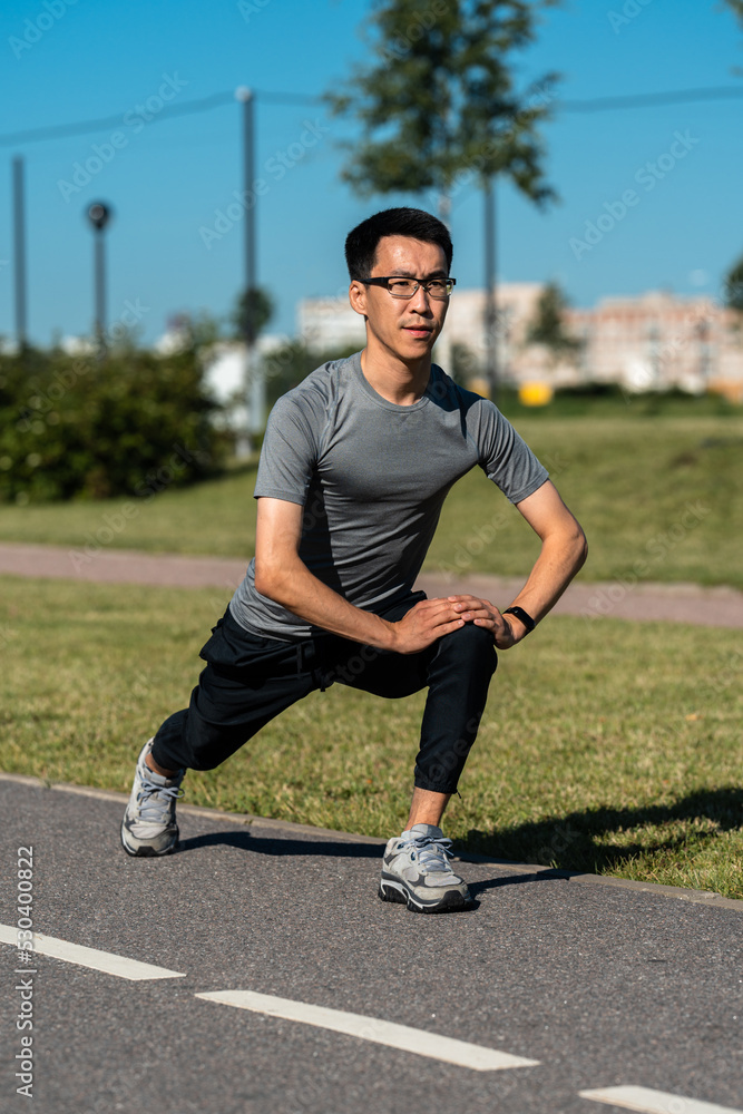 Adult asian man doing exercises, warm up before jogging in park.