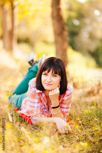 Smiling young woman with black hair lying on the grass in park in summer