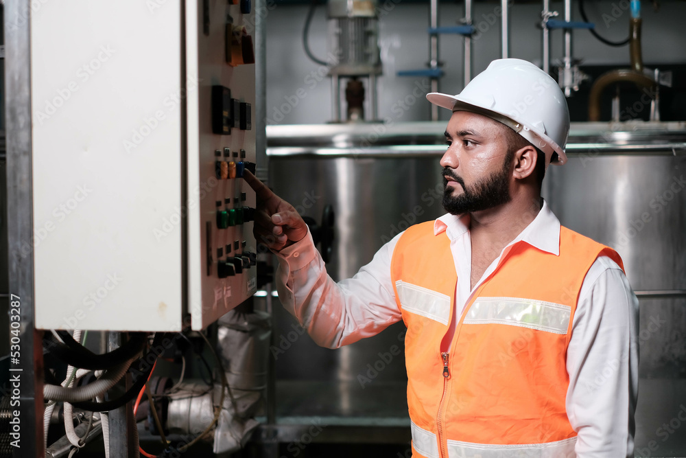 engineer worker working with safety uniform and white helmet to work in industry factory handle tablet. Factory worker inspecting production line of drink production in factory. indian men engineer worker working with safety uniform and white helmet to work in industry factory handle tablet. Factory worker inspecting production line of drink production in factory. indian men