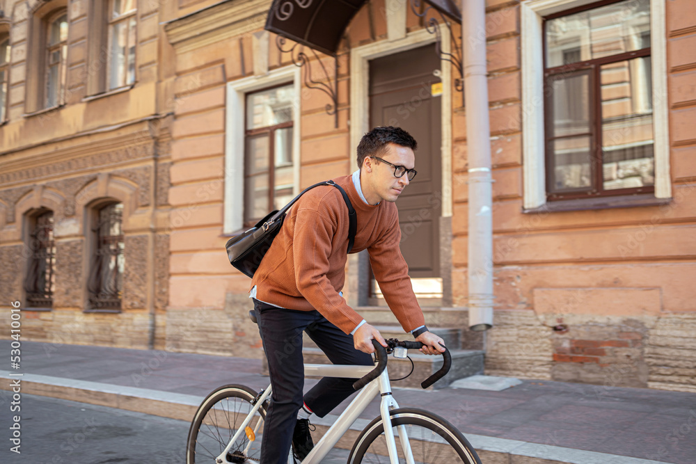 A cyclist with a briefcase rides a bicycle in the city to work.