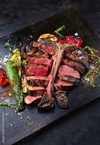 Traditional barbecue dry aged wagyu porterhouse beef steak bistecca alla Fiorentina with grilled vegetable and spice sliced and served as close-up on an old rustic board