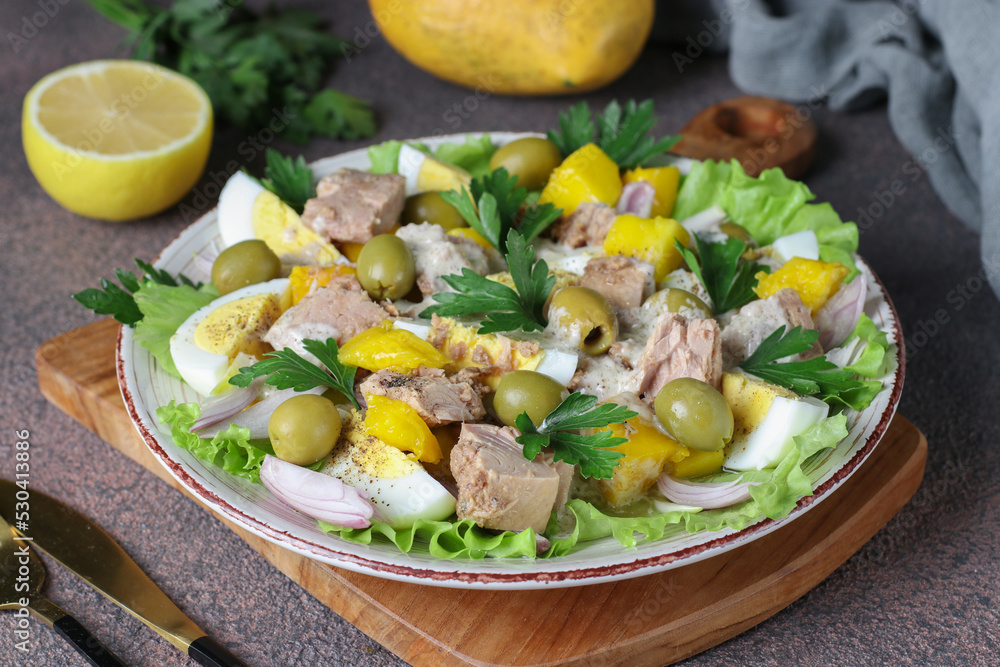 Salad with mango, tuna, eggs and olives served with green lettuce leaves in plate on brown background Salad with mango, tuna, eggs and olives served with green lettuce leaves in plate on brown background