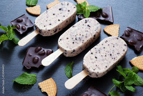Creamy popsicle on a dark background, next to pieces of chocolate and mint leaves