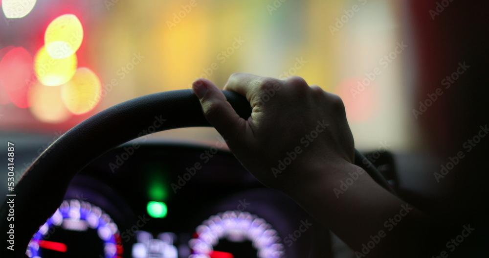 Commuter hand closeup driving at night holding car steering wheel