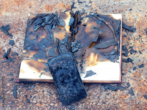 Charred phone and book on a metal surface after a fire photo