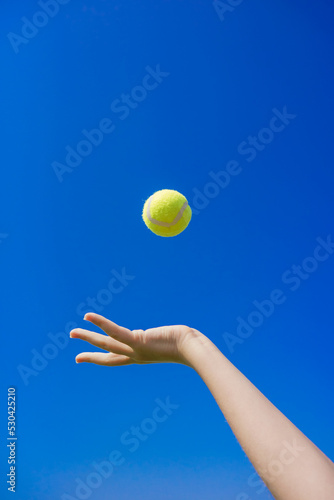 A hand threw a tennis ball into the sky. Hand throwing up a tennis ball to serve against a blue sky background. Sports gear for tennis © Світлана Л.