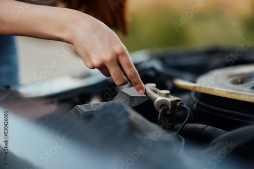 A woman traveler stands by her old car with the hood open and repairs the car engine with a wrench 