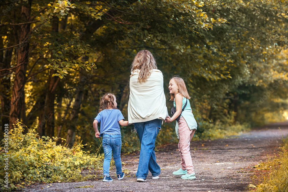 mom and her two little daughters hold hands and walk together along the path of the autumn park. family active vacation on warm autumn days mom and her two little daughters hold hands and walk together along the path of the autumn park. family active vacation on warm autumn days