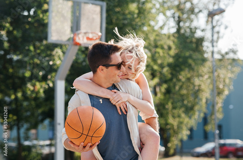 summer holidays, love and people concept - happy young couple with ball having fun on basketball playground