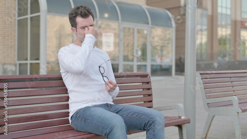 Young Man with Headache Sitting Outdoor on Bench