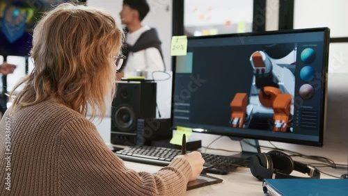 Caucasian female artist designer in glasses draws on a tablet a 3D model of a dog robot for a computer game in the office of a project development studio. Then she turns to the camera and smiles.