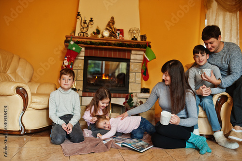 Happy young large family at home by a fireplace in warm living room on winter day.