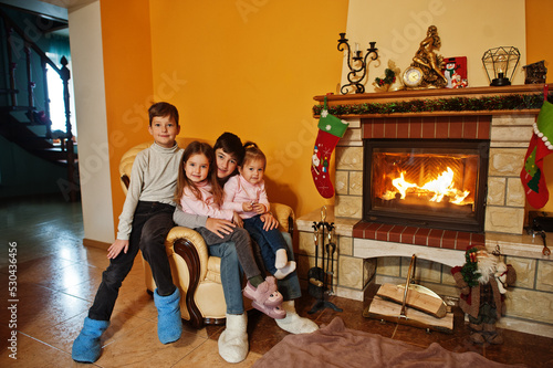 Happy four kids at home by a fireplace in warm living room on winter day.