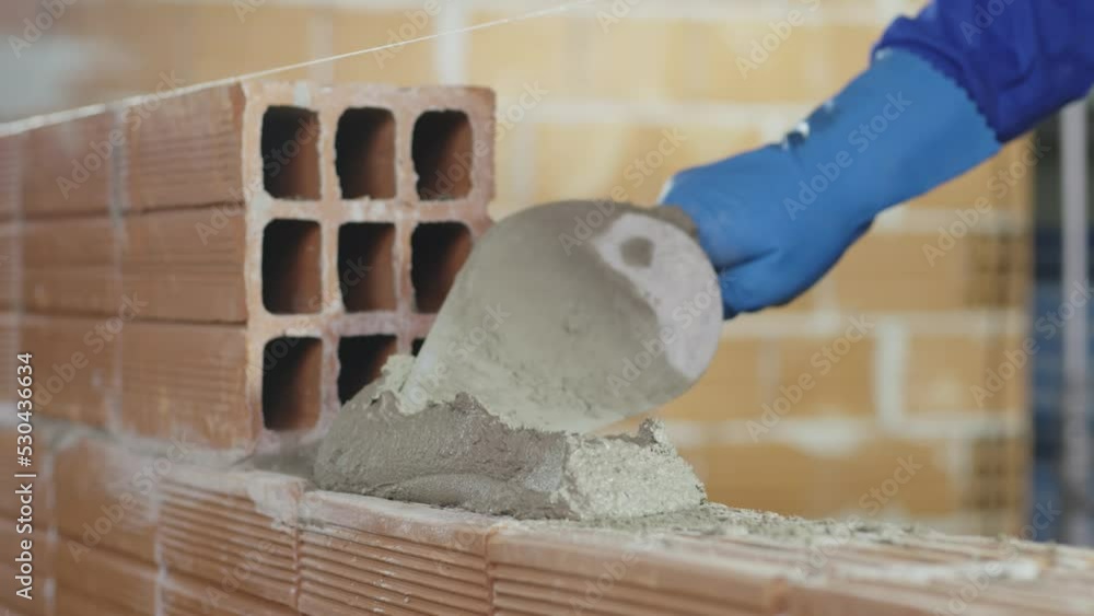 Pedreiro assentando tijolos com cimento em obra. Construção de casa ou prédio.