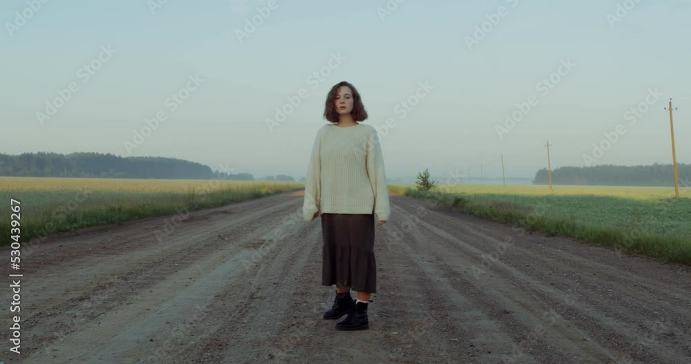 A young red-haired woman in a wet skirt stands on a gravel road among picturesque fields and looks into the camera with a confused look. 4k video, red komodo A young red-haired woman in a wet skirt stands on a gravel road among picturesque fields and looks into the camera with a confused look. 4k video, red komodo