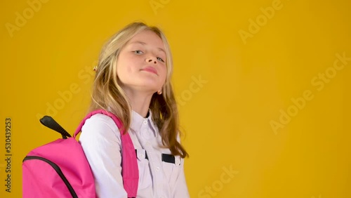 Portrait of a happy teenage schoolgirls in a school uniform with a backpack smiling on a yellow studio background. back to school concept	