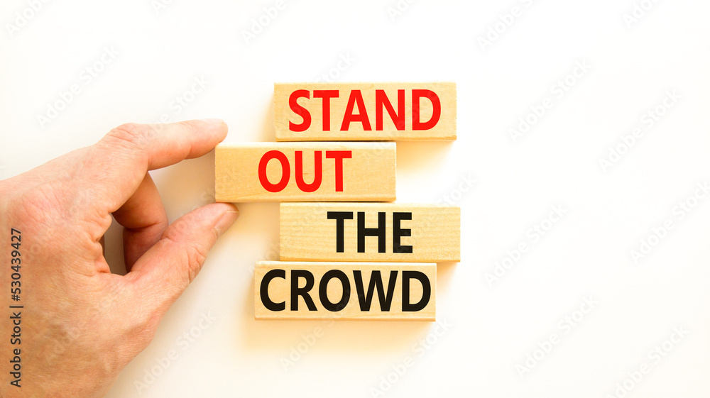 Stand out the crowd symbol. Concept words Stand out the crowd on wooden blocks on beautiful white table white background. Businessman hand. Business, stand out the crowd concept Stand out the crowd symbol. Concept words Stand out the crowd on wooden blocks on beautiful white table white background. Businessman hand. Business, stand out the crowd concept