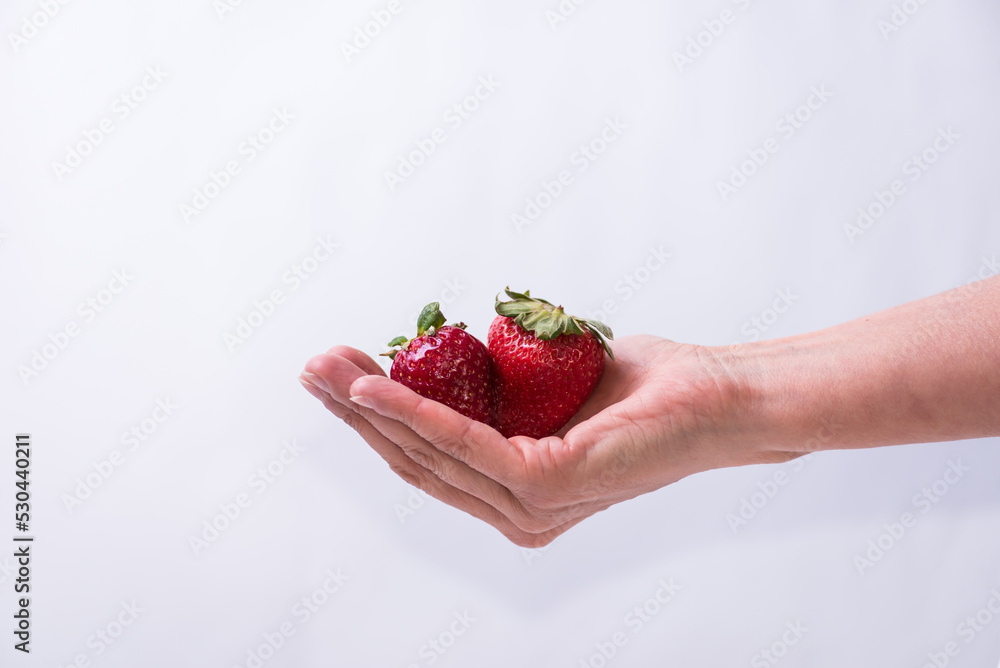 Obraz premium delicate hand holding two red strawberries, fruit, healthy living, lifestyle, healthy lifestyle