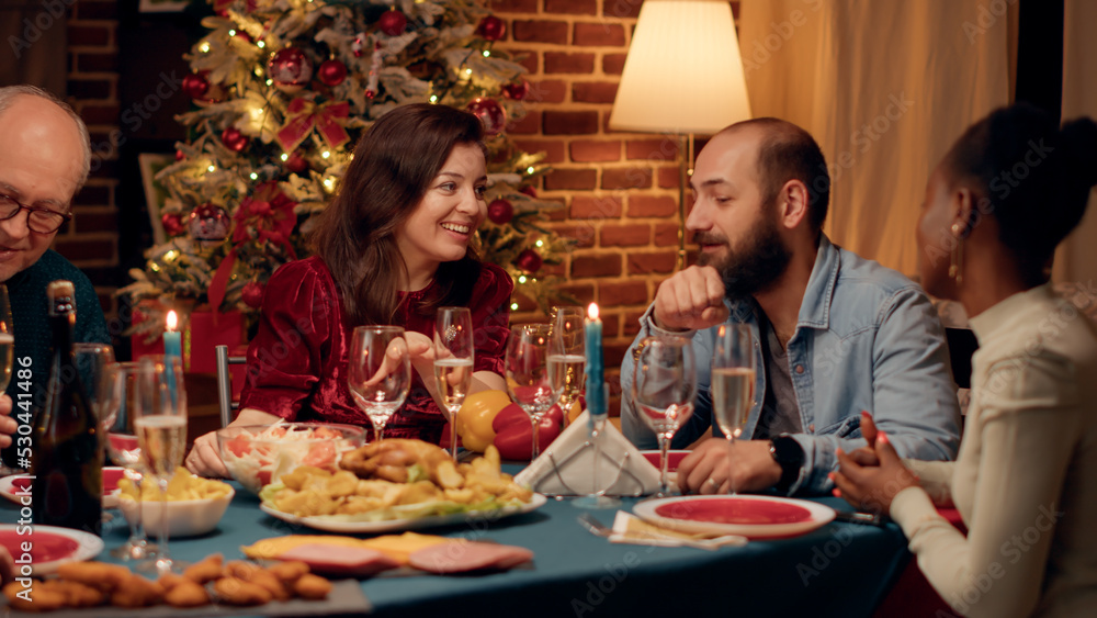 Joyful wife and husband talking at home while enjoying Christmas dinner together. Lovely happy multiethnic group of people being festive while celebrating winter holiday.