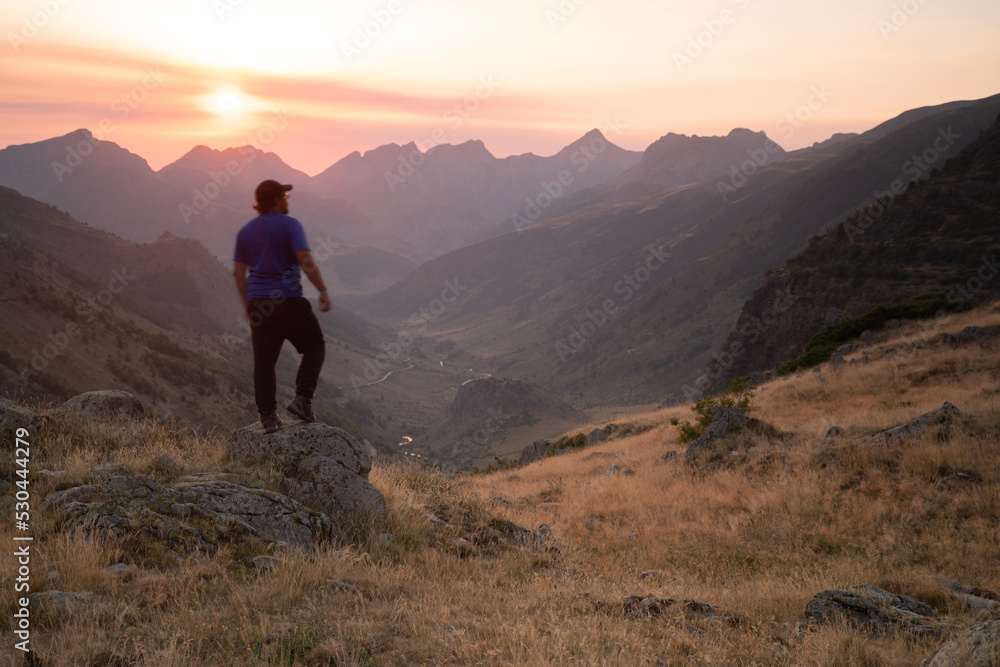 man standing on a mountain summit looking to the red sunset