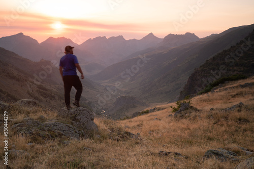 man standing on a mountain summit looking to the red sunset