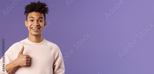 Close-up portrait of satisfied young smiling man recommend something really good, show thumbs-up in approval, like and agree with perfect choice, leave positive feedback, smiling happy photo