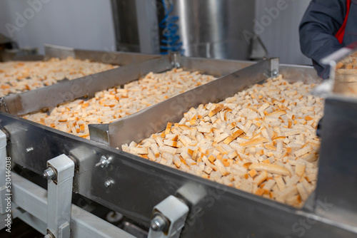 Sliced bread in metal containers on conveyor belt. One of stages of making crackers or croutons. Automated line for production of rusks from bread. Conveyor line machine