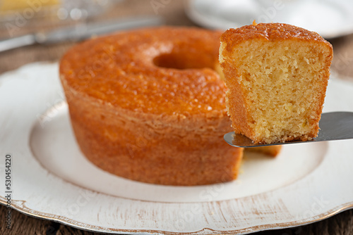 Homemade round cornmeal cake, typical Brazilian food made from corn in a June party and dish on a rustic wooden table with selective focus on the slice on the spatula photo