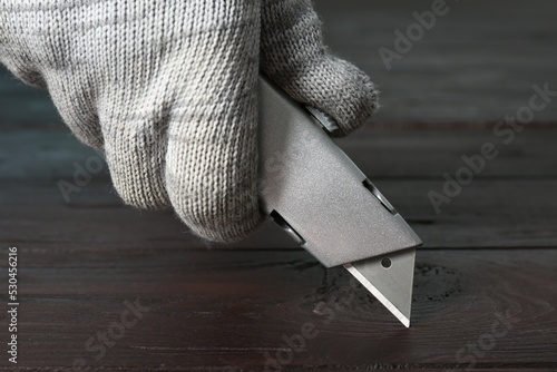 Man using utility knife at wooden table, closeup photo