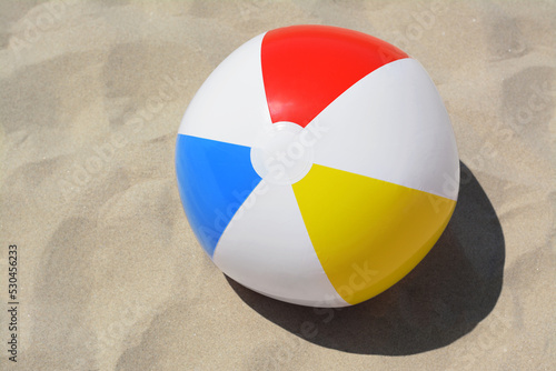 Colorful beach ball on sand, above view