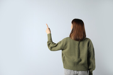 Young girl pointing on white background, back view. Space for text