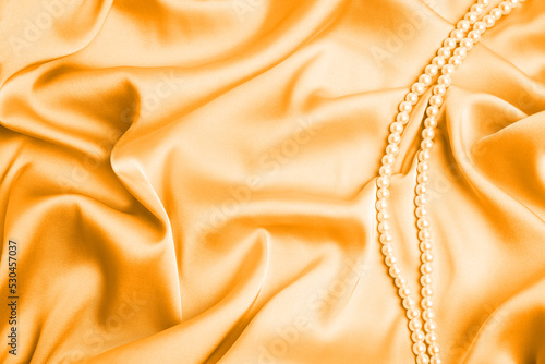 Beautiful pearls on light orange silk, top view