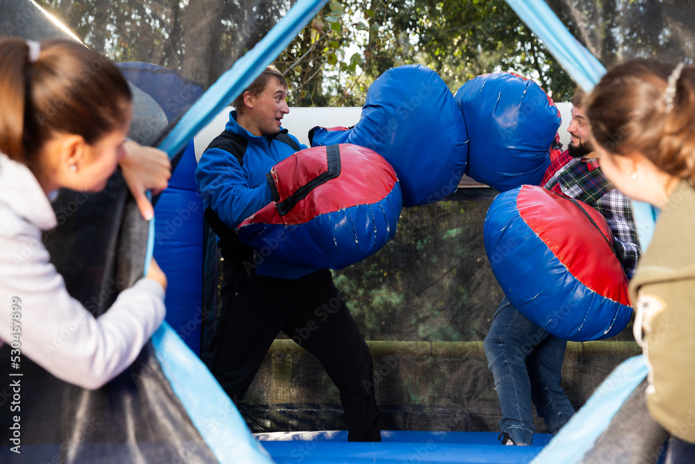 Obraz premium Happy male friends fighting by big stuffed boxing gloves at outdoor amusement playground