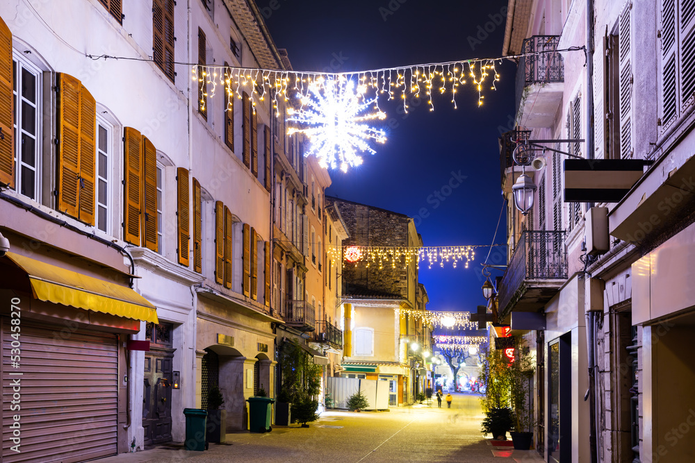 Scenic view of central street of small French town of Montelimar with bright colorful Christmas light decorations on winter twilight, Drome department