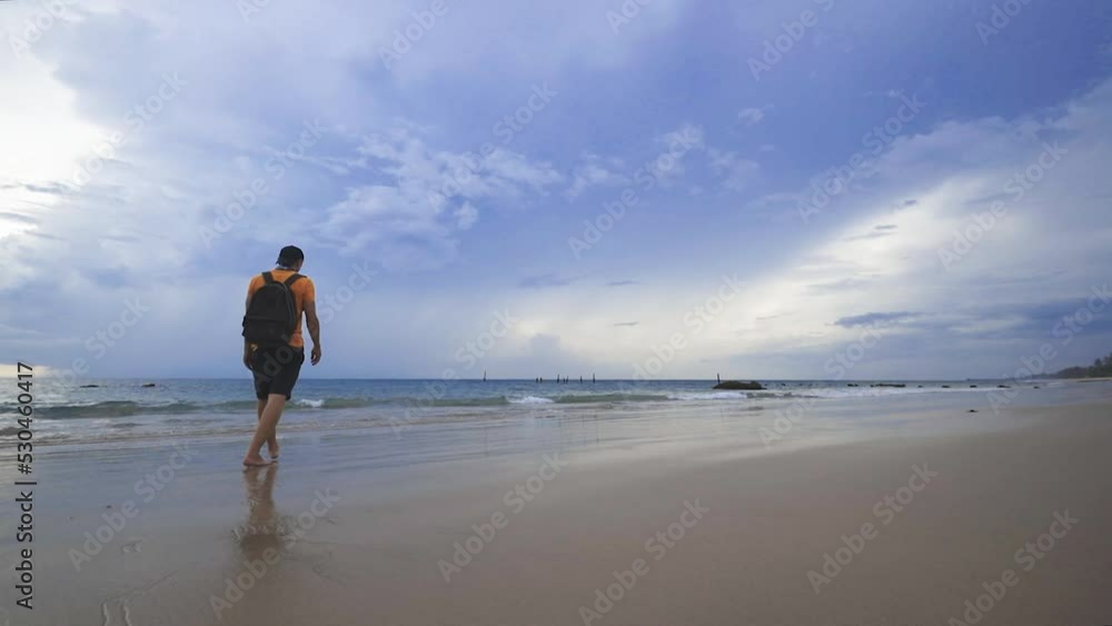 Man walks on beach towards the sea barefoot, Thailand Man walks on beach towards the sea barefoot, Thailand