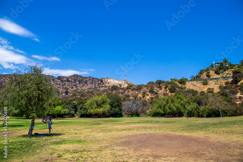 a gorgeous summer landscape in the Hollywood hills with the Hollywood sign on the hillside surrounded by lush green trees, grass and plants with a radio tower and a gorgeous clear blue sky