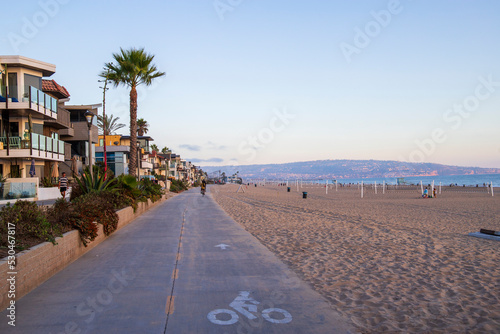 a long smooth bike path along the beach with people riding bikes surrounded by silky brown sand and beachfront homes and lush green palm trees and plants in Manhattan Beach California USA photo